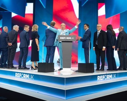 Reform UK leader Nigel Farage, flanked by other key members of his party, on a stage behind a podium Reform UK leader Nigel Farage, flanked by other key members of his party, on a stage behind a podium