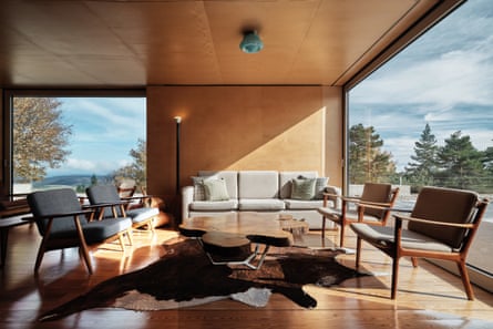 A sunny interior with wooden floors and ceiling, upholstered wooden armchairs and views of trees through floor-to-ceiling windows
