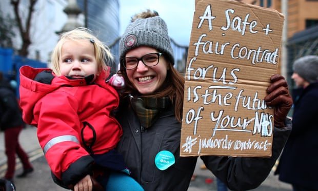 A junior doctor holds her baby and a placard outside Kings College hospital in London.