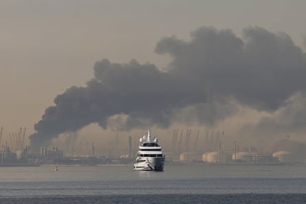 Smoke rising in background as yacht sails in foreground
