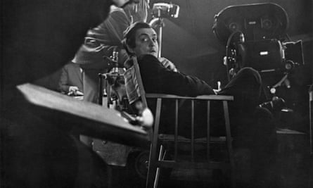 Fotografía en blanco y negro de un hombre sentado en una silla rodeado por un equipo de cámara.