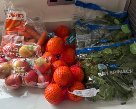 Bags and packs of apples, oranges and baby spinach on a kitchen worktop.