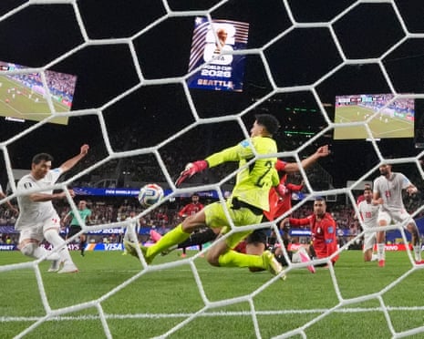 An Iranian football player kicks the ball towards the Egypt goal keeper as their teammates watch beneath a screen reading ‘World Cup 2026’.