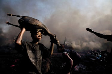 50 Years of Oil in the Niger Delta 2004 – 2006A fourteen-year-old boy transports the carcass of a freshly killed goat, which has been roasted by the flames of burning tires at Trans Amadi Slaughter in Nigeria, 2006.