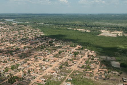 Aerial view of pink, sandy roads and homes in a grid next to a deep cut of dark green jungle.