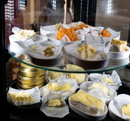 A glass cabinet with little pats of butter in paper cases, some yellow, some greenish, some orange