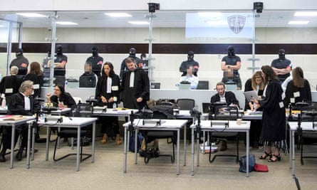 Lawyers prepare for a court session during the trial, with the accused sitting behind glass.