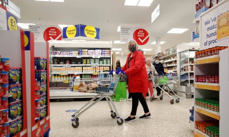 A woman wearing a face mask pushes a shopping trolley at a Tesco supermarket