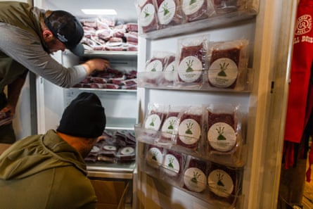 Two people restocking a fridge with packed meat.
