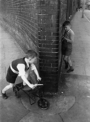 One young boy ambushing another around a street corner, each holding his toy gun at the ready.