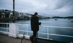 A man with his back to the camera holds a fishing rod over the side of a pier.