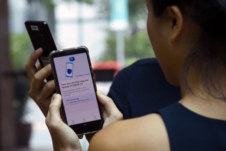A woman in singapore looks at a smartphone with the contact-tracing app on it.