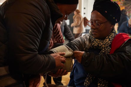 A black woman wearing a hat sits in a chair having her blood pressure taken by another woman