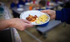 An adult hands a plate of sausage and egg to a child