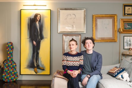 Thompson sits on a sofa next to a man in his 20s. On the wall behind them are framed portraits, a painting and line drawings.