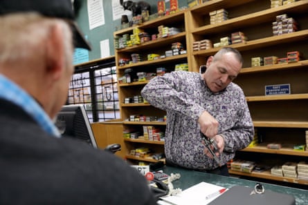 man wearing patterned shirt holds gun as man wearing hat looks on