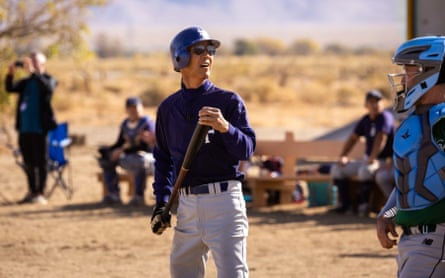 Organizer Dan Kwong holds a bat on a baseball field, standing near a catcher