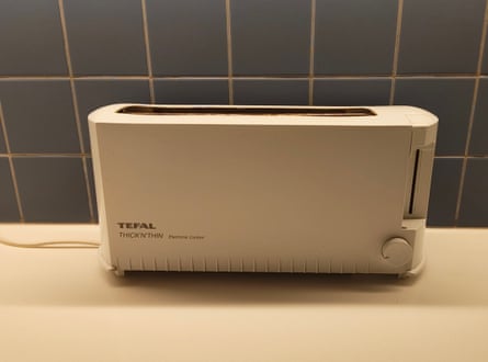 A white toaster sits on a cream worktop with dark tiles behind it
