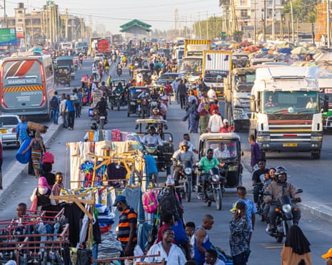 A busy road with people, market stalls, buses and trucks