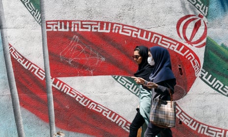 Iranians walk past a mural of Iran’s national flag in Tehran