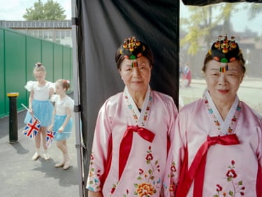 Backstage, (from the series DONGPO), 2024In this vivid portrait by British-Korean photographer Chan-yang Kim, two cultures meet within the frame. Dressed in vibrant Korean hanbok, Jung-sook and Soon-hee were preparing to perform a traditional fan dance when the two young dancers behind passed by. The girls’ Union Jack flags and bright blue tutus echo the shades of the tied ribbons and embroidered flowers decorating Jung-sook and Soon-hee’s hanboks, creating a harmonious image of cultural contrasts