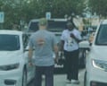 a man and a woman stand between cars in a parking lot