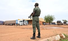 A Nigerien police officer stands guard in Niamey next to trucks, mainly loaded with food, that have arrived from Burkina Faso