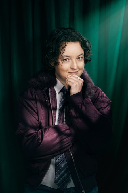 A smiling person with a hand to their chin wearing a plum-coloured padded jacket