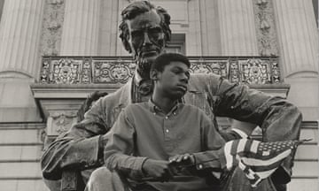 A Black boy holding a US flag sits on the lap of an Abraham Lincoln statue.