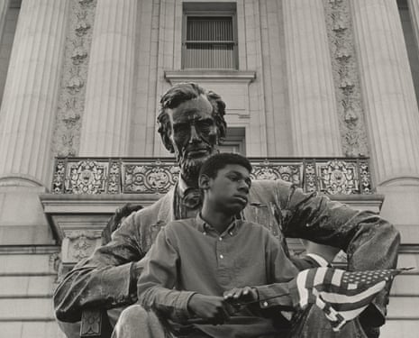 A Black boy holding a US flag sits on the lap of an Abraham Lincoln statue.