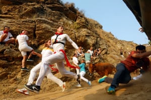 Men, some dressed in white and red outfits, run down a path or scramble to the side as a bull chases them