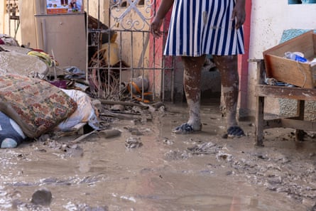 woman in striped dress stands in mud surrounded by debris