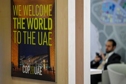 A poster saying ‘We welcome the world to the UAE’ displayed on a wall with a man texting on his phone in the background