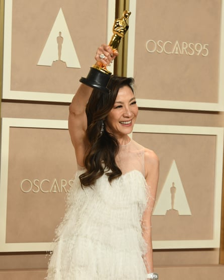 Michelle Yeoh holds her Oscar high in the air, smiling