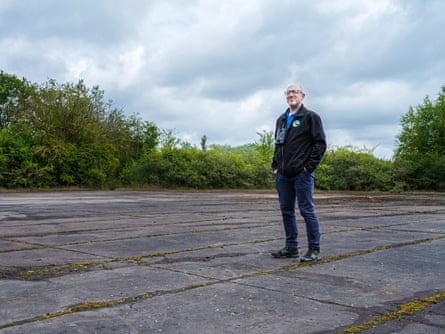 Man stands on grey asphalt surface, at the edges of which is greenery.