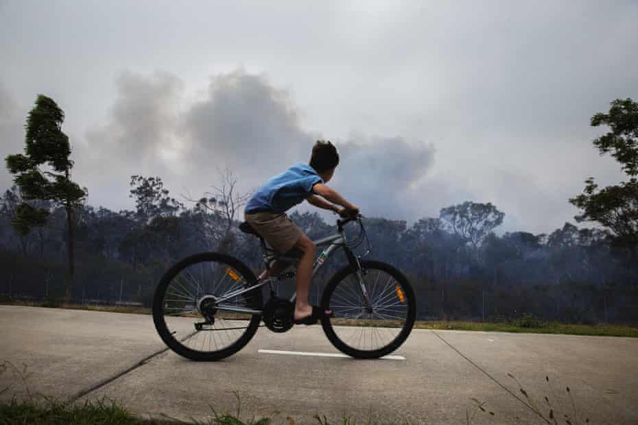 A boy on a bike looks on as a fire smoulders at Voyager Point in Western Sydney.