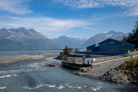 A large building sitting on a riverbank with mountains looming in the background