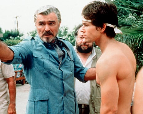 Jack Horner gestures while speaking to a shirtless Dirk Diggler wearing a headband