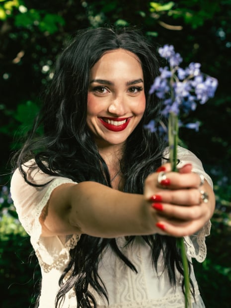 Bella Hull smiles, holding purple bluebell flowers toward the camera