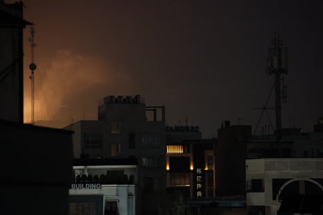 A view of Tehran at night with smoke rising behind buildings.