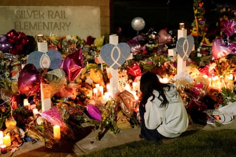 A person crouches beside a memorial of flowers, candles and crosses outside Silver Rail Elementary