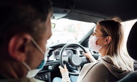 A woman during a driving lesson with her instructor, both wearing face masks