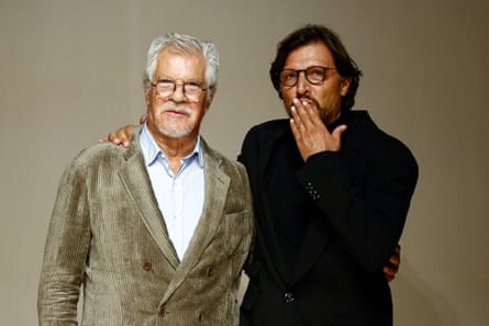 Leo Dell’Orco, wearing a light green velvetine blazer and white shirt stands next his nephew Gianluca, wearing a black blazer and who is blowing a kiss to someone.