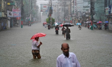 People with umbrellas walk through water above their knees.