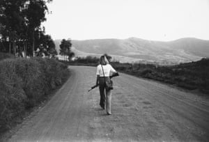 A woman walks down a dirt road with hills in the background, carrying a rifle in 1979 Rhodesia (now Zimbabwe)