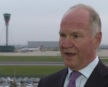 He speaks wearing shirt and tie and with the control tower in the background