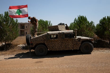 A soldier adjusts a Lebanese flag on an armored vehicle.