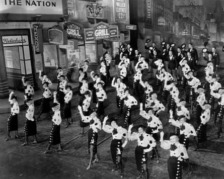 Dozens of women pose in synchronicity, showing their stocking tops, on a New York street set