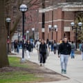 People walking on a sidewalk on a college campus, with brick buildings
