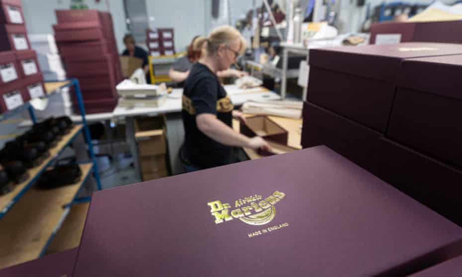 A Dr Martens shoe box and behind it a woman opening another shoe box at the factory near Wellingborough